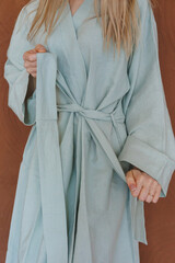 A woman is elegantly dressed in a light blue robe that is tied around her waist, showcasing a beautiful and comfortable garment choice