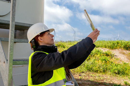 Female engineer using digital tablet maintaining wind turbine in green field