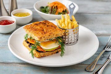 Gourmet vegetable sandwich with fresh herbs and fries on the side