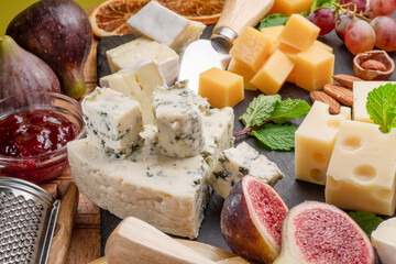 Variety of sliced cheeses with fruits, mint, nuts and cheese cutting knives.