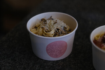 Carbonara pasta with bacon in a round cardboard takeout box