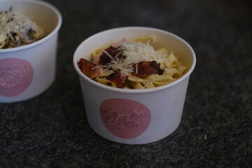 Carbonara pasta with bacon in a round cardboard takeout box