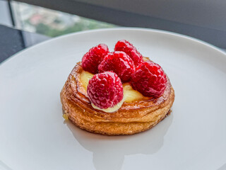 Closeup Of A Cream Tart Topped With Sugar Glazed Raspberries On A White Plate