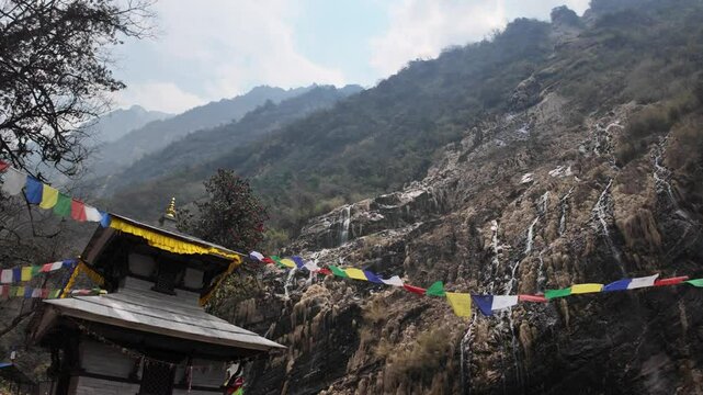 Pojenghem Baraha Waterfall Temple decorated with colorful prayer flags in Annapurna Base Camp trek, Nepal. Foggy and misty himalayan mountains during the day.