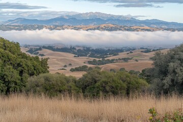 Misty valley nestled within rolling hills.  A mountain peak rises above the clouds