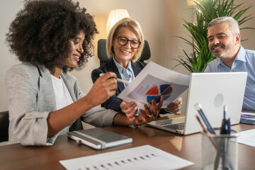 Three busy happy middle aged professional business man and two women executive leaders team using laptop working on computer at work desk having conversation on financial project at meeting in office.