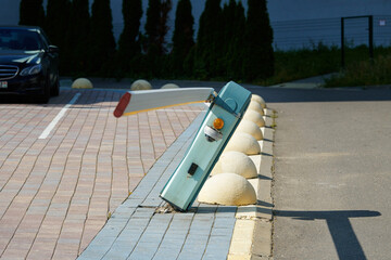 Damaged automatic barrier gate, parking lot boom barrier with torn out fastenings from the sidewalk. Broken automated barrier parking system, damaged boom gate in parking lot.