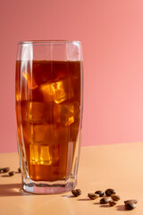 Ice coffee with coffee beans in a tall glass on pink background.