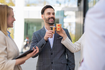 Happy business team toasting with takeaway coffee cups during a casual outdoor meeting, smiling and enjoying a light moment together.
