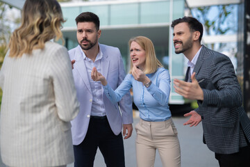 Angry group of office colleagues arguing with a female coworker outdoors, demonstrating workplace tension, conflict, and interpersonal issues among employees