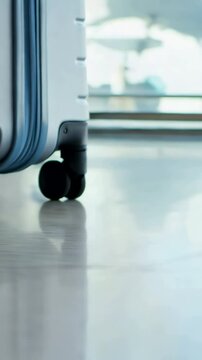 Close-up of black wheels of silver hard-shell suitcase rolling quickly on light floor, suitable for travel vlogs or luggage promotional videos