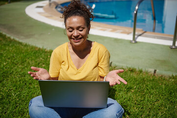 Woman Using a Laptop Outdoors by the Pool on a Sunny Day