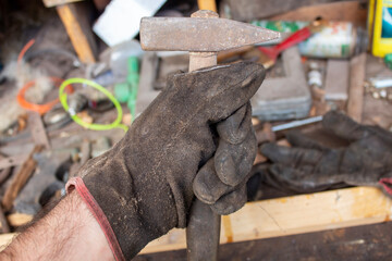 Close-up of a gloved worker’s hand firmly holding a hammer in a cluttered workshop. A perfect symbol of labor dedication and strength, ideal for Labor Day tributes and promotions.