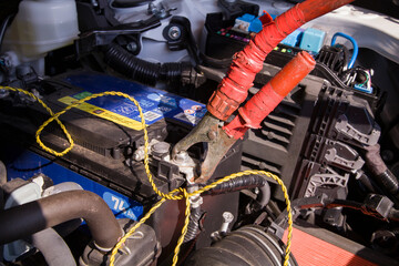 A bulky red jumper cable clamp connected to the positive battery terminal, clearly visible under the open hood of a car