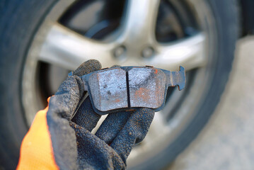Mechanic holds in hand bad brake pad, replacing worn uneven defective pads. Vehicle brake system service, brake pad replacement. Car maintenance. Selective focus