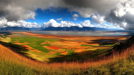Obraz premium Panoramic view of a valley with colorful farmland, a lake, and mountains