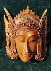 An intricately carved wooden mask depicting a serene face and elaborate headdress, Southeast Asian...