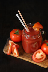 Tomato juice on a dark background. Vegetable diet drink. Fresh tomato juice in a glass with a handle. Ripe red tomatoes and juice made from them. Glass with juice and a straw, tomatoes. Healthy drink