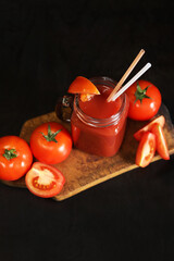 Tomato juice on a dark background. Vegetable diet drink. Fresh tomato juice in a glass with a handle. Ripe red tomatoes and juice made from them. Glass with juice and a straw, tomatoes. Healthy drink