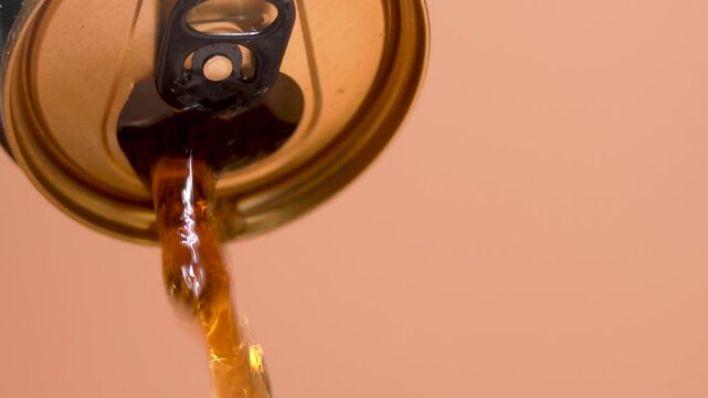 A soda drink is pouring out of a can. A can with a carbonated drink on a brown background. The can is open and a carbonated drink is pouring out of it.