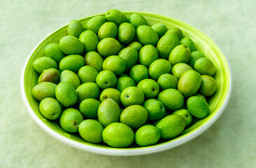 Beautiful kitchen plate with fresh green olives on monochrome green salad background. Olive dish closeup, foor and drink concept