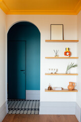 Close-up details of a stylish home interior. Wooden shelves with handmade vases and jugs, books and incense sticks. Elegant blue wooden doors and an arched hallway passage