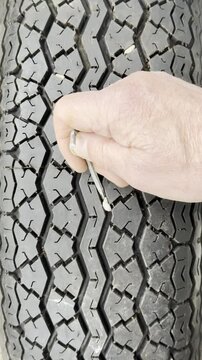 Vertical video social media - Closeup slow motion shot of a man&rsquo;s hand using a hex or allen key to prise and remove a small stone from the tread of a vehicle tyre or tire.