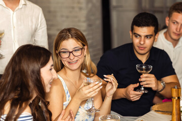 Young people at a party are eating and drinking champagne. Cute girls chat and drink cocktails at a friendly meeting.