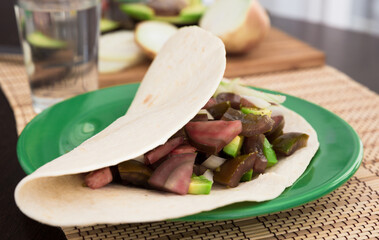 Salad of black tomatoes, avocado and onions in Italian tortilla on green plate