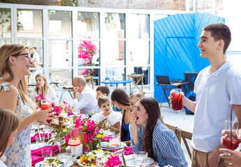 Young people at the festive table raise their glasses. A smiling boy congratulates a beautiful laughing girl on her birthday.