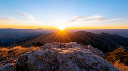 Obraz premium Mountain peak vista with sunburst at dawn, golden light, rocky foreground