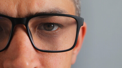 A detailed close-up focuses on a person's eye behind black-framed glasses. The reflection on the...