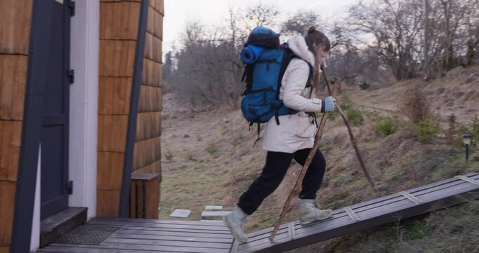 Girl in hiking clothes with big blue backpack holding hiking wooden poles and going on a hike outside the city from home. Travel outside the city