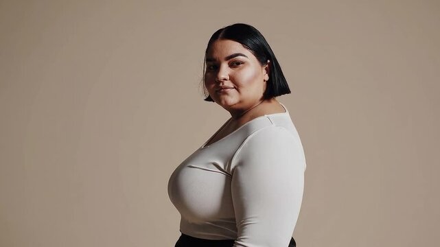 A plus-size Caucasian woman standing confidently in a studio setting, wearing casual clothing such as jeans and a loose sweater.