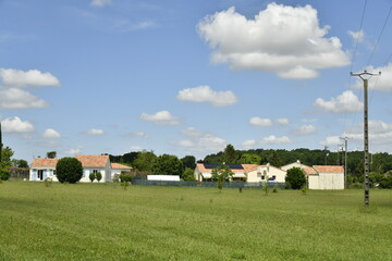 Obraz premium Pelouse sous des cumulus de beau temps près d'un lotissement rural au bourg de Champagne au Périgord Vert 