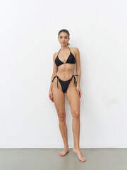 Striking model showcases confident pose in sleek black bikini in fashion studio setting