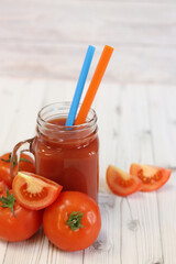 Delicious tomato juice in a glass and fresh tomatoes on a light gray table. Tomato juice on a light background. Fresh juice in a glass with a handle. Glass with juice and a straw. Vegetable drink
