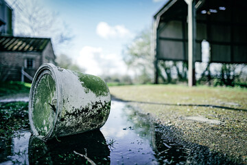 Shallow focus of a discarded agricultural chemical bucket seen lying in an oil slick on a derelict...
