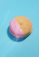 Single Macaron Cookie with Pink Dip on Blue Background