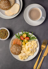 Food photography of keto breakfast with scrambled eggs and sandwich with low-carb bun with smoked salmon, tomato, arugula, smoked cheese scamorza and coffee cappuccino