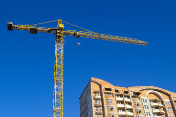 An unfinished building and a construction crane against the background of a sky.
