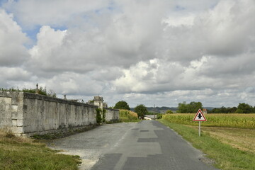 Fototapeta premium Route longeant le mur d'enceinte d'un cimetière typique sous un ciel gris près du bourg de Vendoire au Périgord Vert 