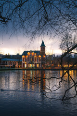 Fototapeta premium Elegant Historic Building by a Lake at Dusk – Reflections and Winter Trees Framing the Scene