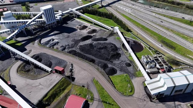 Drone view of a large coal processing and storage facility with conveyor belts and nearby highways in an industrial area.