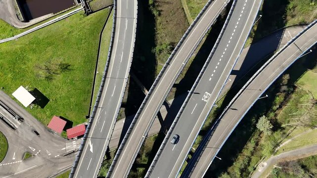 Drone top-down view of a complex highway intersection with merging lanes, surrounded by green fields and infrastructure.