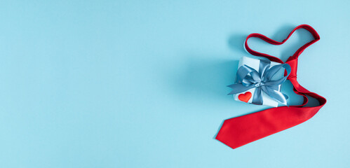 Happy Fathers Day background. Flat lay, top view of red heart shaped necktie, gift box and red heart on blue background.