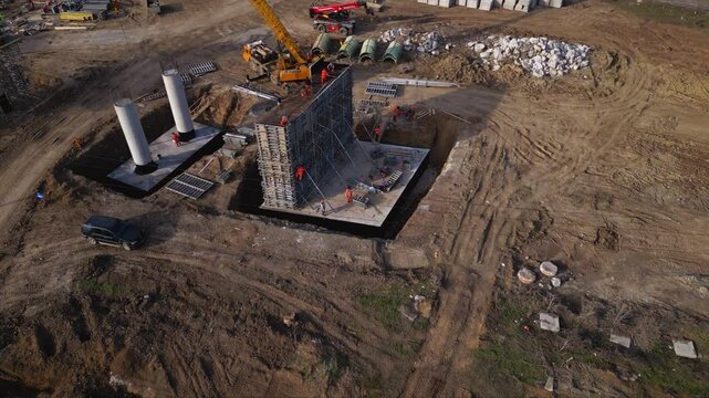 Aerial footage of workers climbing and working on a concrete formwork with scaffolding during the construction of a bridge pier column. Drone shot of labour at a worksite of highway project.
