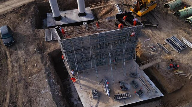 Aerial footage of workers climbing and working on a concrete formwork with scaffolding during the construction of a bridge pier column. Drone shot of labour at a worksite of highway project.
