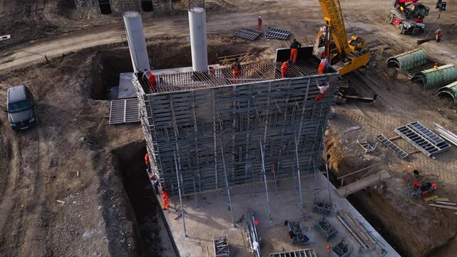 Aerial footage of workers climbing and working on a concrete formwork with scaffolding during the construction of a bridge pier column. Drone shot of labour at a worksite of highway project.
