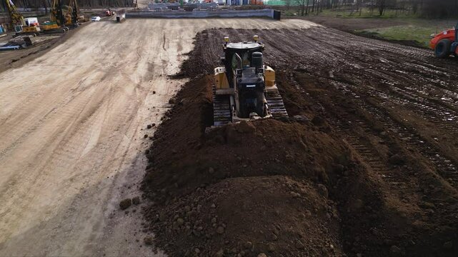 High angle footage of bulldozer leveling dirt in layers during a highway construction project. Heavy machinery pushing earth around a build site for a road. drone shot of soil compacting works.

